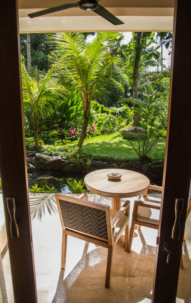 阳台的豪华巴厘岛酒店与看出去的门，椅子和桌子站在郁郁葱葱的绿色热带后院图片下载