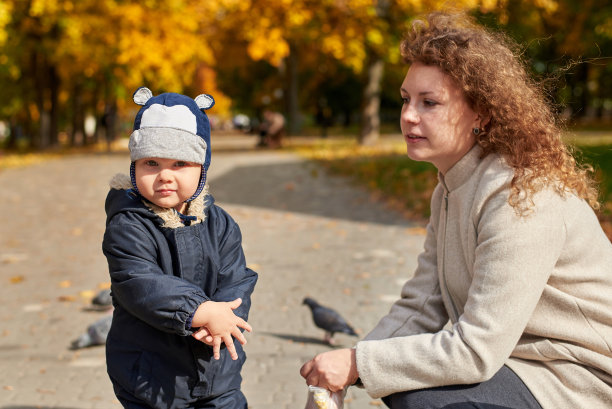 秋天，带着儿子的妈妈在公园里喂鸽子。图片下载