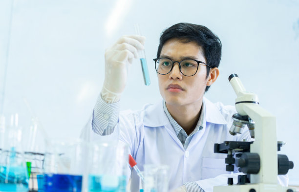 近距离的亚洲科学家男子坐在桌子上，戴着防护手套，以持有试管烧瓶后，混合科学的液体溶液从烧杯在实验室房间的医疗保健和制药概念的研究和开发图片下载