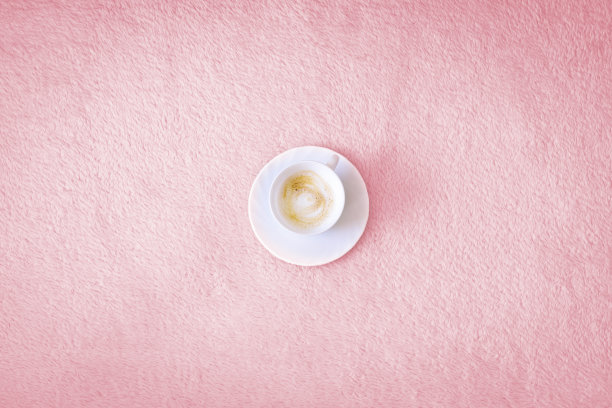 粉红色背景下的一杯咖啡。一杯装在白色杯子里的卡布奇诺放在粉红色的床罩或地毯上图片下载