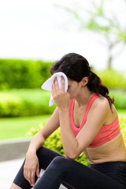 美丽的女子跑步者已经使用白色毛巾擦拭她的脸后，在花园里跑步。图片下载