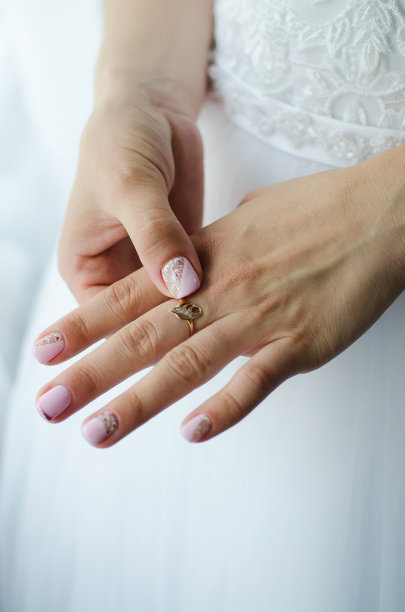女性手的特写，手指上戴着结婚戒指。穿着婚纱的新娘。垂直的摄影。图片下载
