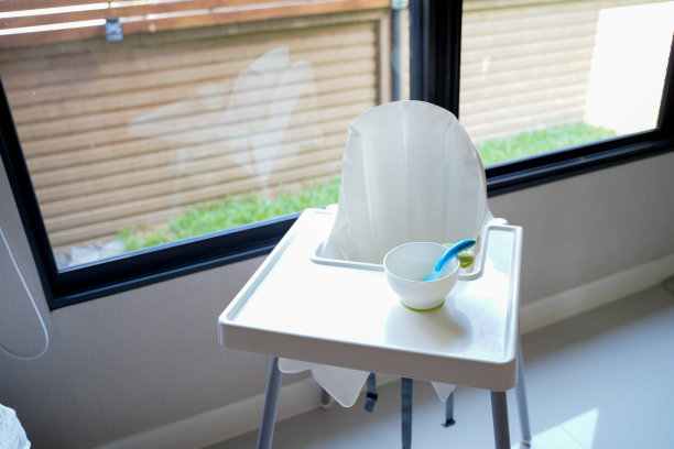 靠近房子窗户旁边的白色高脚椅，一个空的白色碗和蓝色的勺子准备给婴儿餐，婴儿喂养概念。图片下载