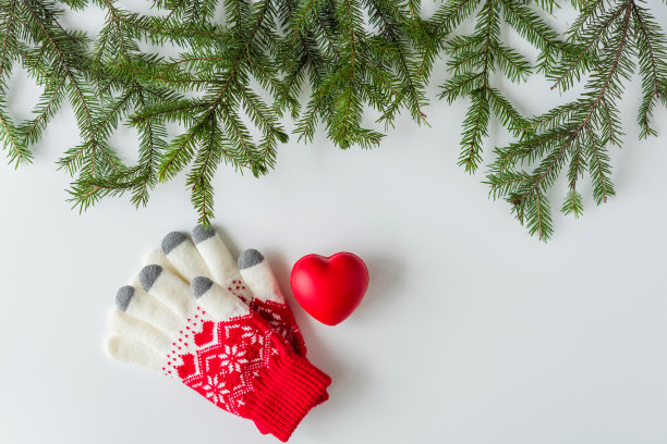 白色的桌子上放着冬手套，上面有一个大大的红心，插在云杉树枝上。圣诞节和新年的概念。平躺，俯视图。图片下载