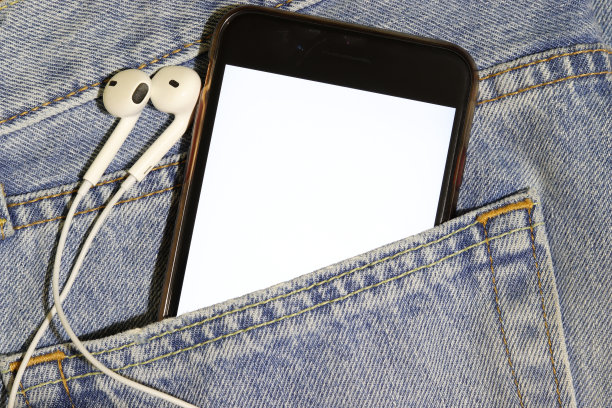 音乐内容的模板。蓝色牛仔裤口袋里有一台白色屏幕和耳机的智能手机。图片下载