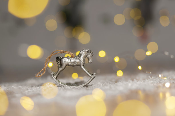 圣诞主题的装饰小雕像。摇摆木马的小雕像。装饰圣诞树。节日装饰，温馨的散景灯。图片下载