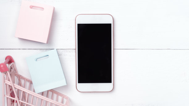 摘要网上购物、移动支付概念设计元素，彩色购物车和纸袋放在白色木质桌子背景上，俯视图，平铺图片下载
