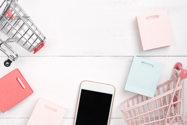 摘要网上购物、移动支付概念设计元素，彩色购物车和纸袋放在白色木质桌子背景上，俯视图，平铺图片下载