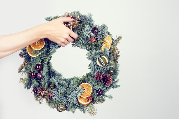特写镜头，一个无法辨认的女人拿着用水果和玩具装饰的香味浓郁的圣诞花环，孤立的背景图片下载