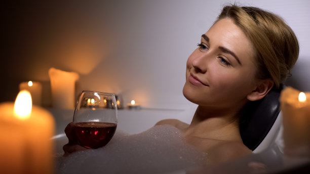 迷人的女人躺在沐浴着泡沫和蜡烛，喝着葡萄酒图片下载