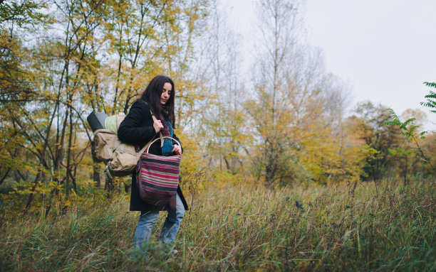 一个穿着大衣背着背包的女孩在秋天的森林里。秋天的概念。图片下载