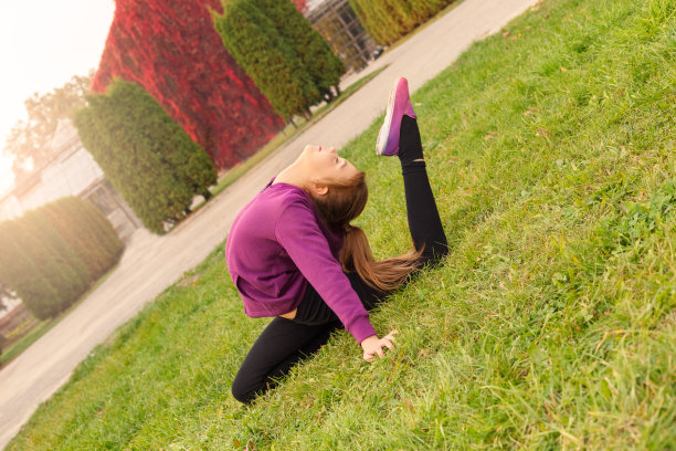 户外休闲。小体操运动员坐着做着体操，弯着腰，在秋天的公园里，闭上眼睛，满心喜悦图片下载