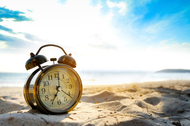 一个新的一天的早晨，闹钟在沙滩上，清晨的阳光。健康和假日的概念。图片下载