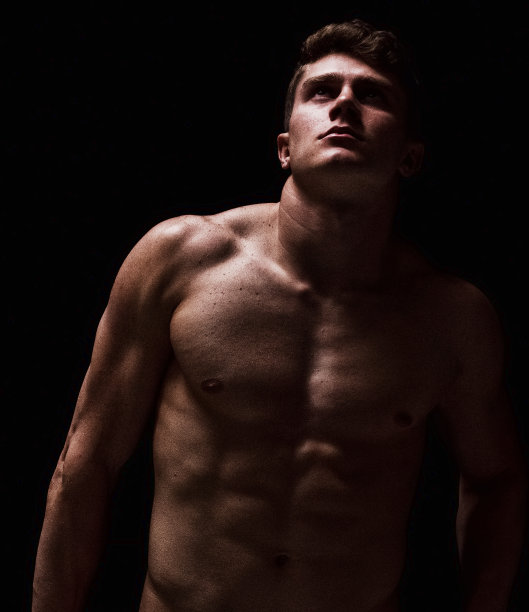 一个男人/一个人/腰部以上/向上看/正面的观点，20-29岁的成年英俊的人白人男性/年轻男子前面的黑色背景，穿着半裙子谁是一个性感的象征/肌肉的建设/赤膊图片下载