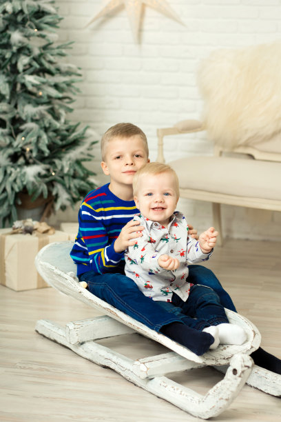 圣诞节已经到了。两个兄弟用圣诞礼盒拉雪橇。可爱的小男孩收到了节日礼物。玩雪橇时，孩子们拿着礼盒。庆祝圣诞节。冬天的活动图片下载