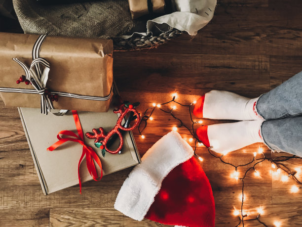 节日快乐。圣诞礼盒，节日灯，圣诞帽和女孩的腿在舒适的袜子在木地板在平安夜。前视图。手机照片图片下载