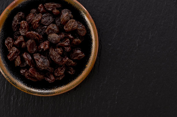 葡萄干在小盘黑石背景图片下载