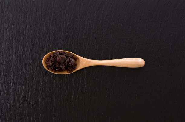 木勺里的葡萄干，背景是黑色的石头图片下载