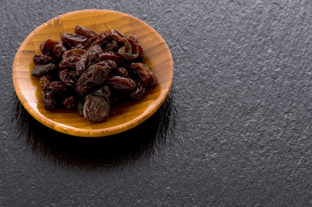 葡萄干在黑色的石头背景的小木盘图片下载