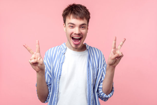 欢乐的棕色头发男子的肖像，小胡子和小胡子显示胜利的标志。孤立在粉红色背景上图片下载