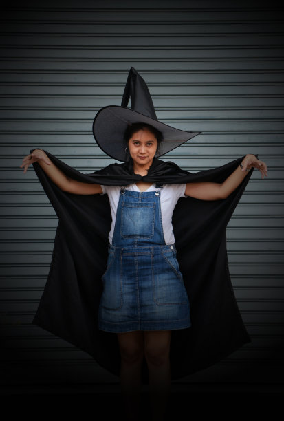 身着黑色斗篷、头戴女巫帽的女子举起双手，在条纹金属背景上展开爪子。图片下载