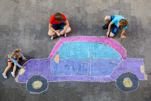 三个小孩，两个学校的孩子男孩和蹒跚学步的女孩在沥青上用彩色粉笔画汽车图片。兄弟姐妹在地上画画，一起玩耍。创造性的休闲图片下载