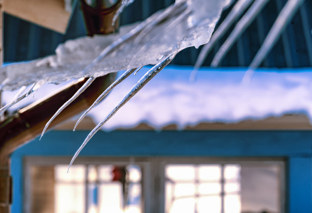 近距离的照片，雪和弯曲的冰柱悬挂在屋顶，模糊的窗户与灯光在背景。瑞典北部。拉图片下载