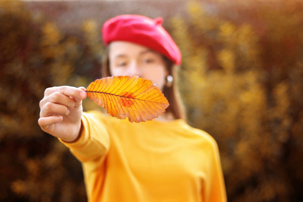 秋天的吻。年轻的女孩戴着红色的帽子，在户外拿着黄色的叶子和红色的口红亲吻邮票。秋天的生活方式。选择性聚焦在叶子上。我喜欢秋天的概念。图片下载