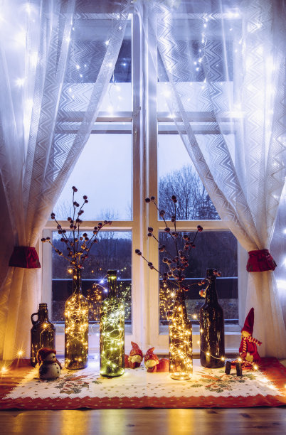 可爱而温暖的圣诞装饰，用复古的啤酒瓶和装满微型led派对灯的葡萄酒瓶，在窗户后面是乡村森林。红色人造浆果的瓶子和花瓶。图片下载