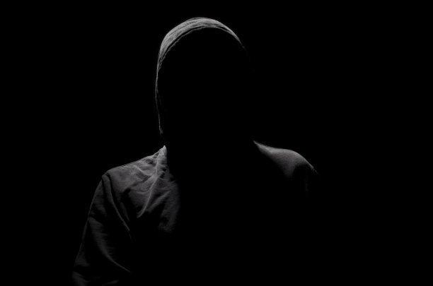 在黑色背景上戴着兜帽的无名人士图片下载