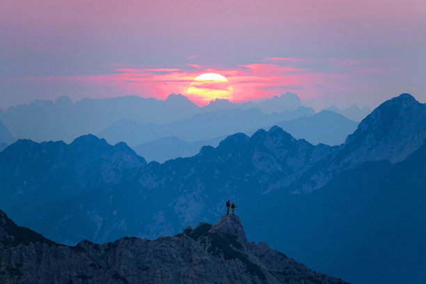 图片:一对徒步旅行者站在岩石山顶上看日出。图片下载