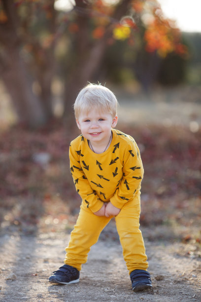 在夕阳西下的秋天，一个穿着黄色衣服的小男孩独自在美丽的公园里的新鲜空气中散步图片下载