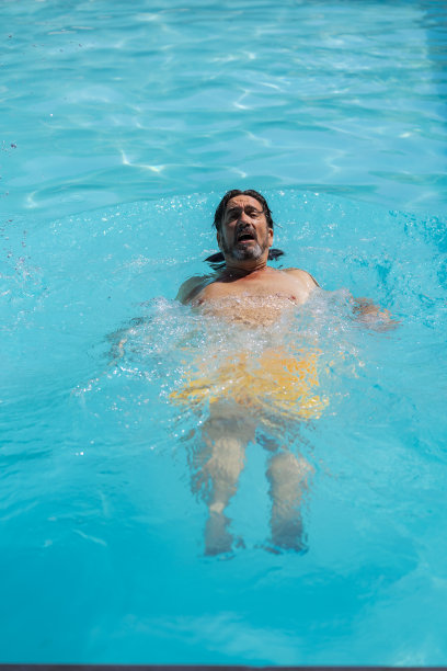 一个男人在游泳池里向后游泳的垂直库存照片。夏季和假期图片下载