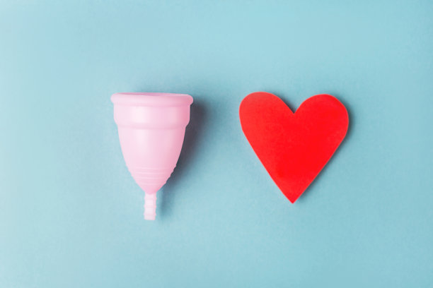 创意月经杯和红心在蓝色的背景。图片下载