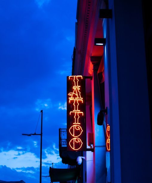 霓虹闪烁的横幅上写着刺青，映衬着蔚蓝色的天空和白云。图片下载