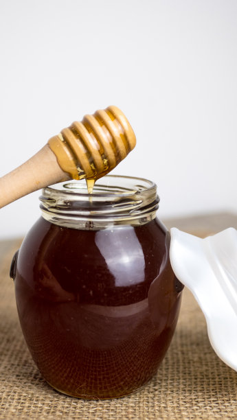 装满蜂蜜的玻璃罐子和白色背景的勺子图片下载