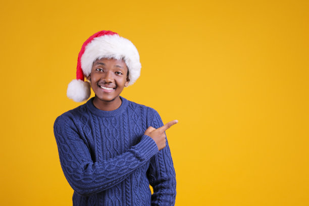 年轻的黑人男性在圣诞老人帽在黄色背景摆姿势。图片下载