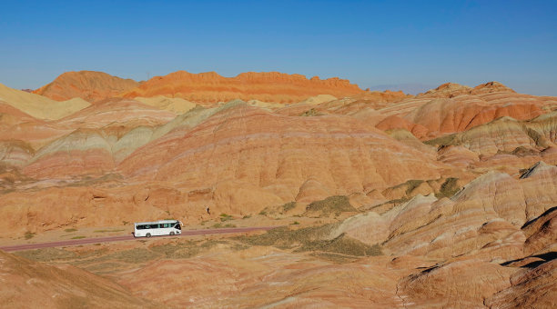 无人机:旅游巴士在穿越丹霞地貌的风景优美的道路上行驶图片下载