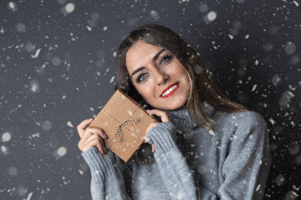 漂亮的年轻女子与礼品包装微笑在黑色的背景图片下载
