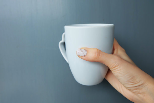 女人手拿着一个浅灰色背景或纹理的杯子。年轻女性拿着咖啡杯与拷贝空间隔离。餐饮设计理念。图片下载