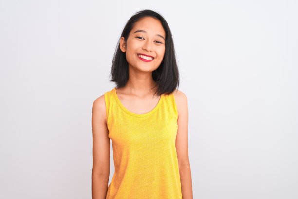 年轻的中国妇女穿着黄色休闲t恤站在孤立的白色背景，脸上带着幸福和凉爽的微笑。幸运的人。图片下载