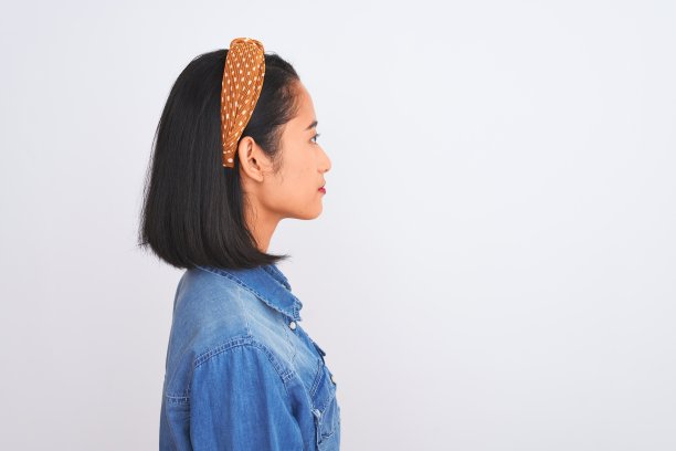 年轻美丽的中国女人穿着牛仔衬衫站在孤立的白色背景看向一边，放松的轮廓姿势与自然的脸与自信的微笑。图片下载