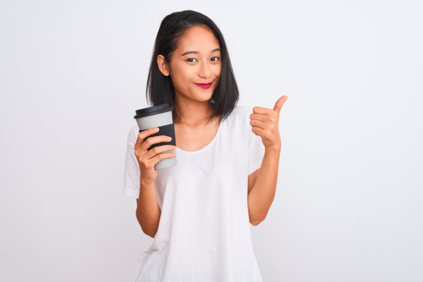 年轻的中国女人喝带走了一杯咖啡，在孤立的白色背景下，开心地笑着做ok的手势，用手指竖起大拇指，优秀的手势图片下载