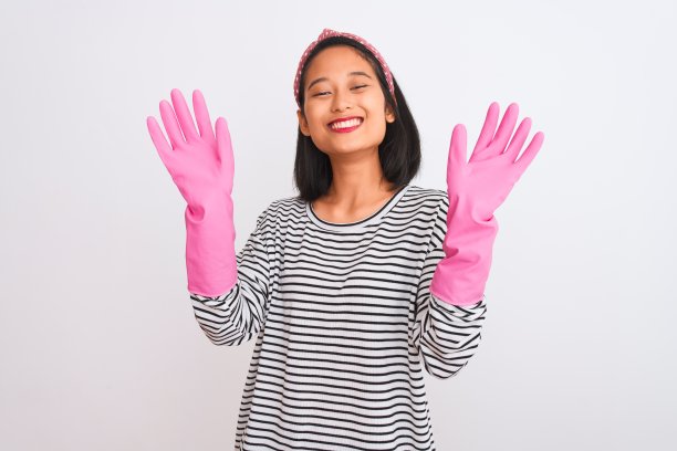 年轻的中国清洁工用手套在孤立的白色背景上清洁，快乐的脸站着，自信的微笑着露出牙齿图片下载