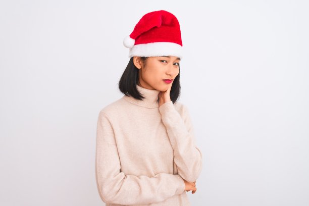 年轻美丽的中国女人戴着圣诞老人的帽子在孤立的白色背景下思考看起来疲倦和厌倦的抑郁问题交叉双臂。图片下载