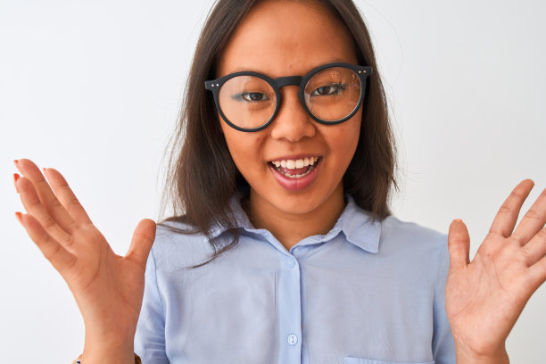 年轻的中国妇女穿着衬衫和眼镜站在孤立的白色背景非常高兴和兴奋，胜利者的表情庆祝胜利尖叫着大大的微笑和举起手图片下载
