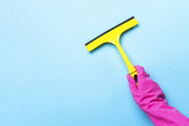 一只戴着粉红色手套的女性手拿着一个刮刀，用来清洁蓝色背景上的窗户。清洁服务理念。平躺，俯视图图片下载