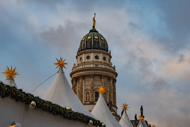 古老大教堂的建筑穹顶和多云的天空在圣诞节期间在欧洲柏林与传统的圣诞装饰节日集市。白色帐篷的顶端有3D黄色星形图片下载