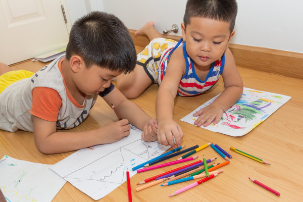 可爱的亚洲男孩躺在地板上给纸上色。图片下载