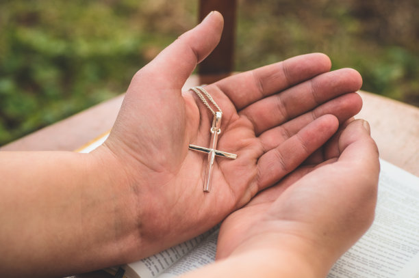 在《圣经》的背景下，一个手里拿着十字架的女人。双手合十祈祷的观念，信仰，灵性和宗教图片下载